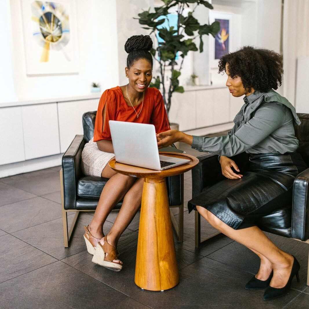 Two woman work together with an laptop and discuss the coachees next steps.