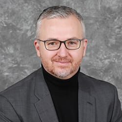 Timothy Tiryaki PCC headshot photo, smiling man in dark business attire and glasses