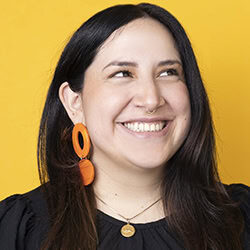 Pame Barba headshot photo, dark haired woman against a yellow background smiling
