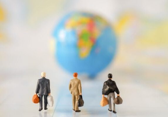 three human figures with bags walking toward a blurred globe