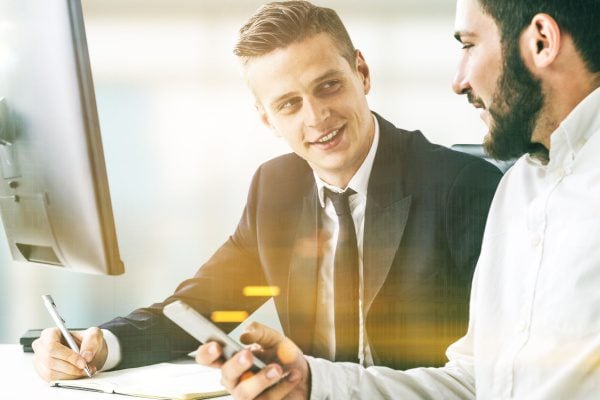 coach and client sitting at a table talking, the coach has a notepad and pen while the client has a cellphone