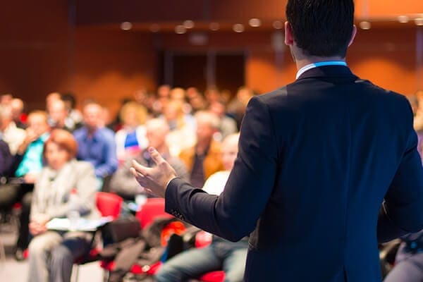 male in a suit speaking to an auditorium
