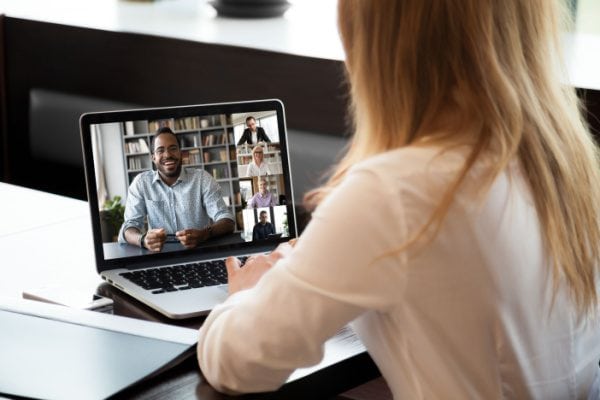 woman videoconferencing with five people on a laptop at a table