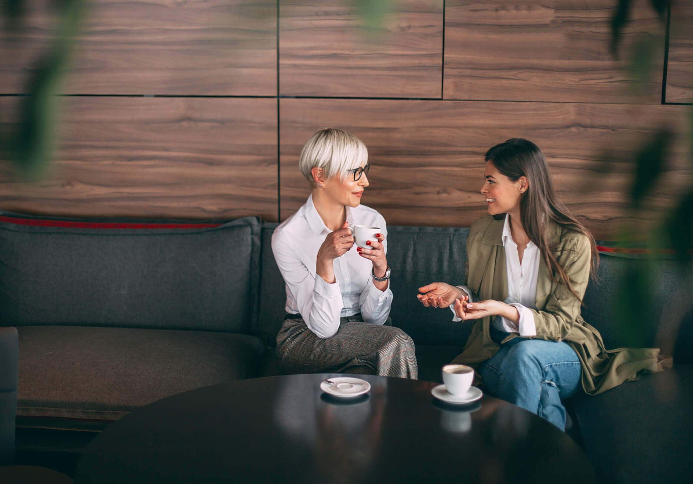 Two women having a coaching session over coffee in a modern lounge.