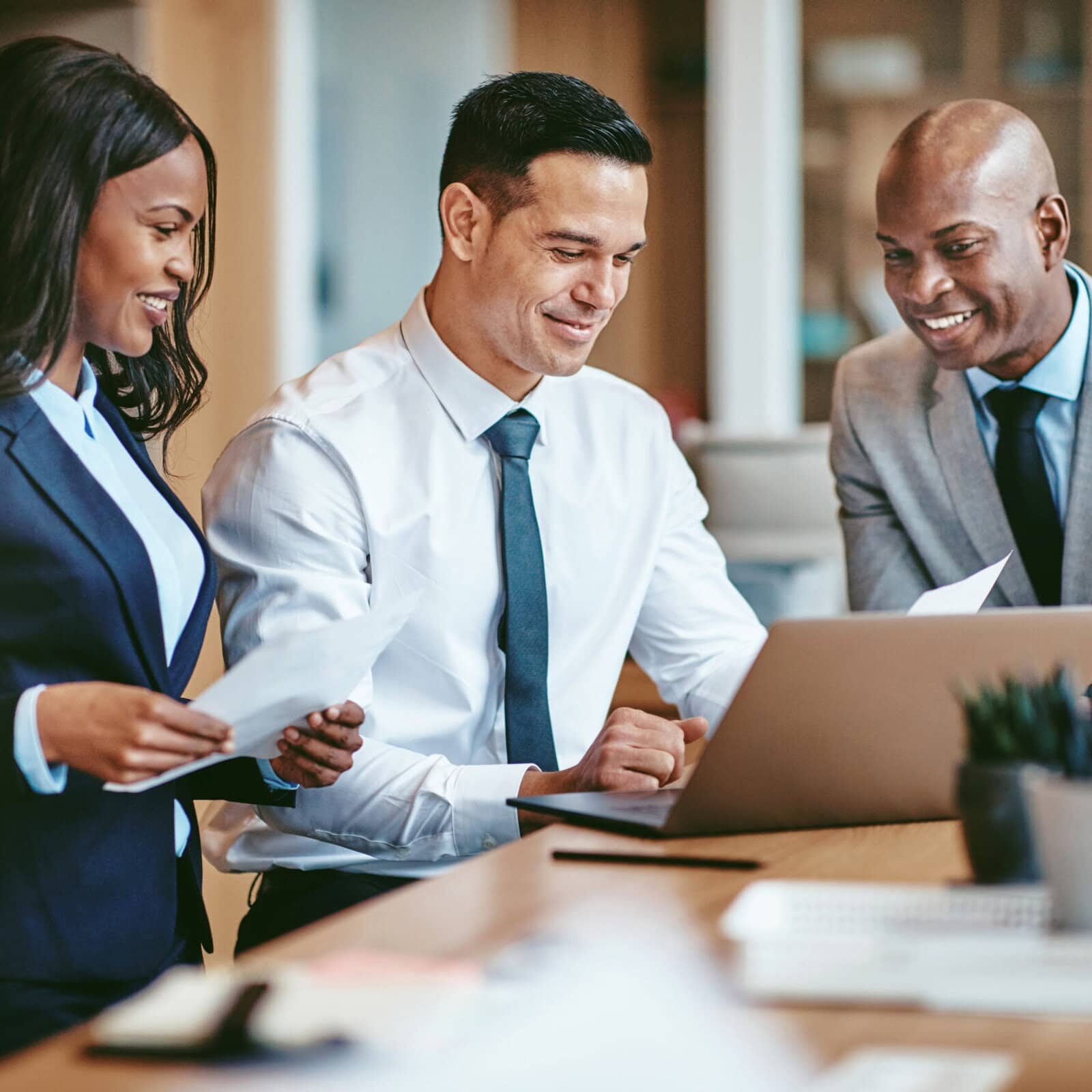 Three professionals — two men and a woman — are all smiling and engaged, suggesting a positive and productive team coaching session.