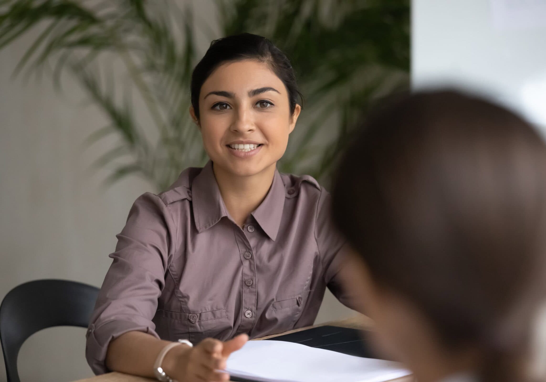 Smiling woman in a violet blouse sitting at a desk and reviewing coaching materials with a student in a modern office.