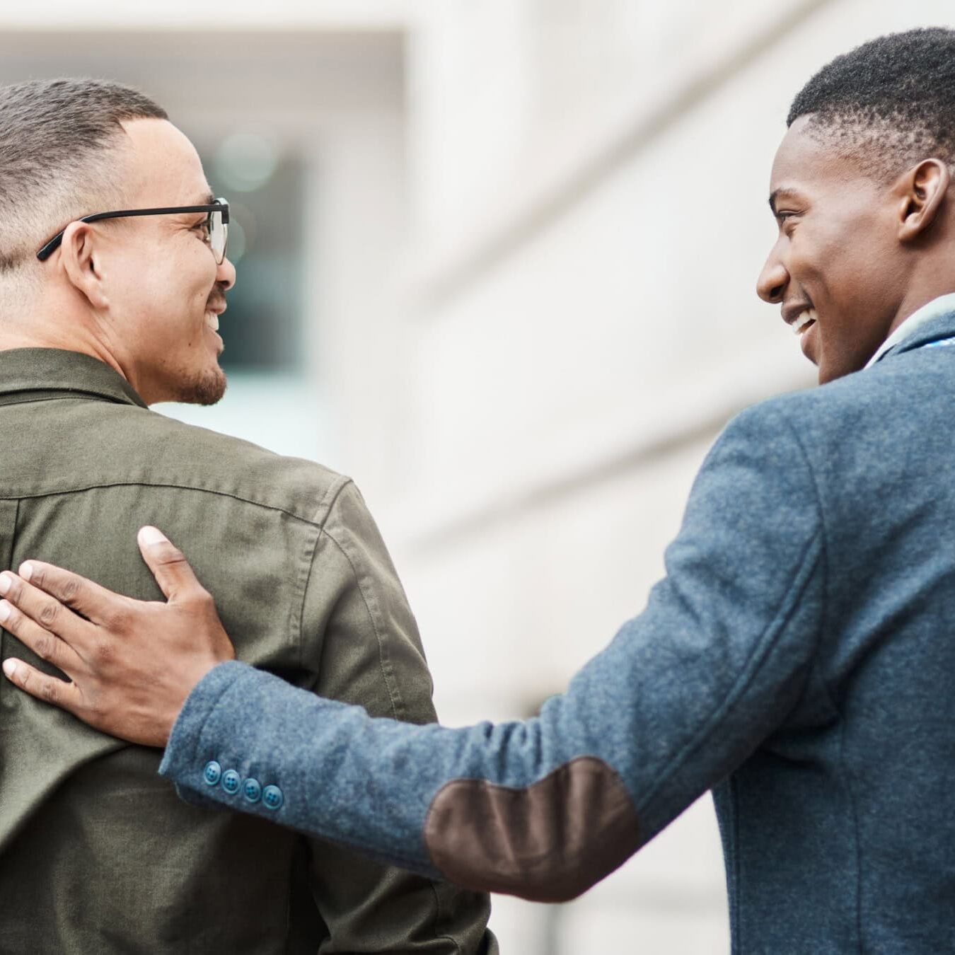 Two men walk outside sharing a casual touch, like they are friends