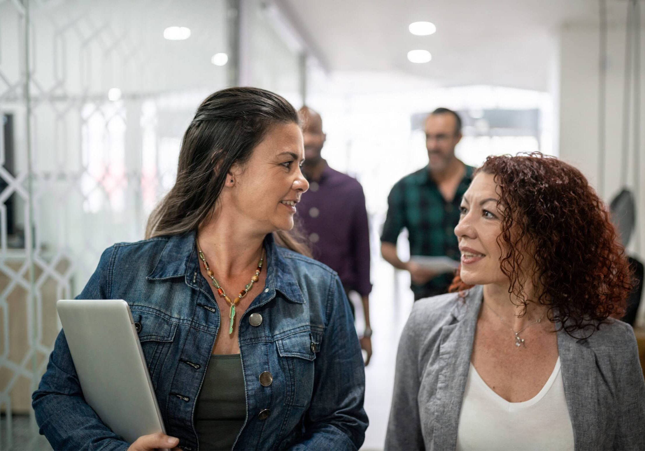 Two women walking and having a collaborative coaching conversation in a modern office, embodying a friendly work environment.