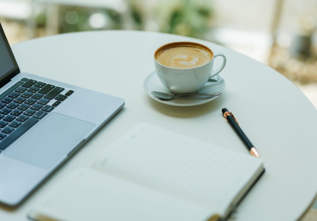 Laptop, notebook, pen, and cup of coffee on a table.