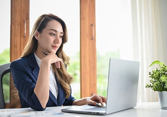 coach in professional attire focusing on her laptop in a light room with a table