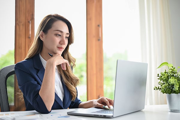 coach in professional attire focusing on her laptop in a light room with a table
