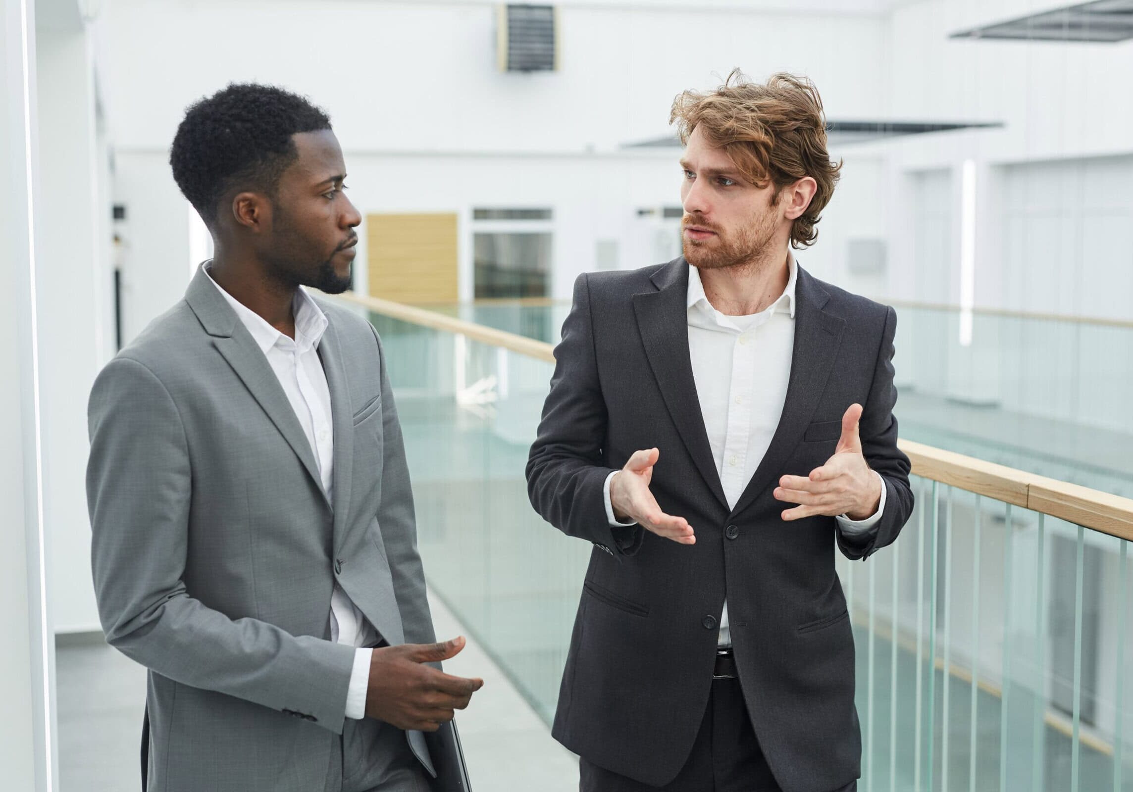 Two young men in suits engaged in an animated professional development discussion in a modern office.