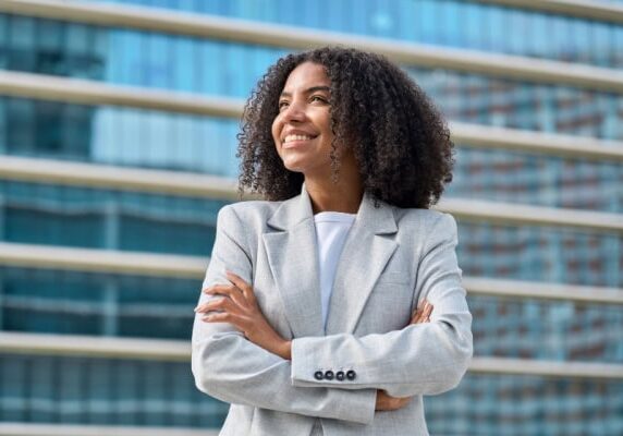woman smiling with arms crossed in front of large office building