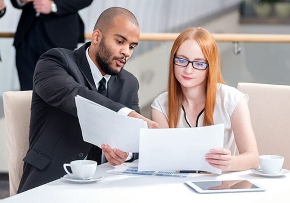 two people at a table looking at paper and one pointing to the paper