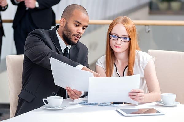 two people at a table looking at paper and one pointing to the paper