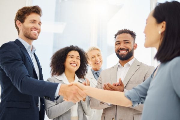 people in a group with one woman shaking a man's hand and everyone looking at the woman