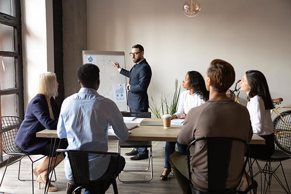 coach using large note pad or white board to lead a group of professionals at a table